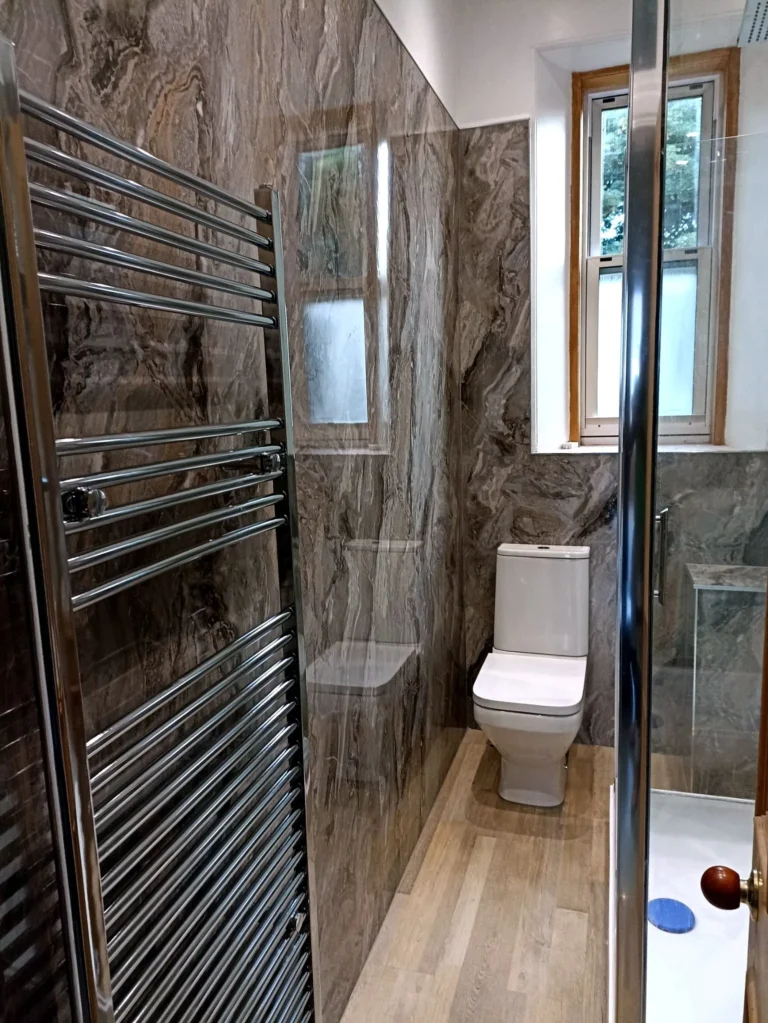 Moka Marmer — chromen handdoekradiator en toilet in smalle badkamer met marmerlook wanden